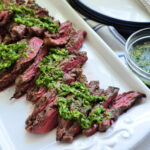 Grilled Sliced Skirt Steak on white platter with Chimichurri Sauce.