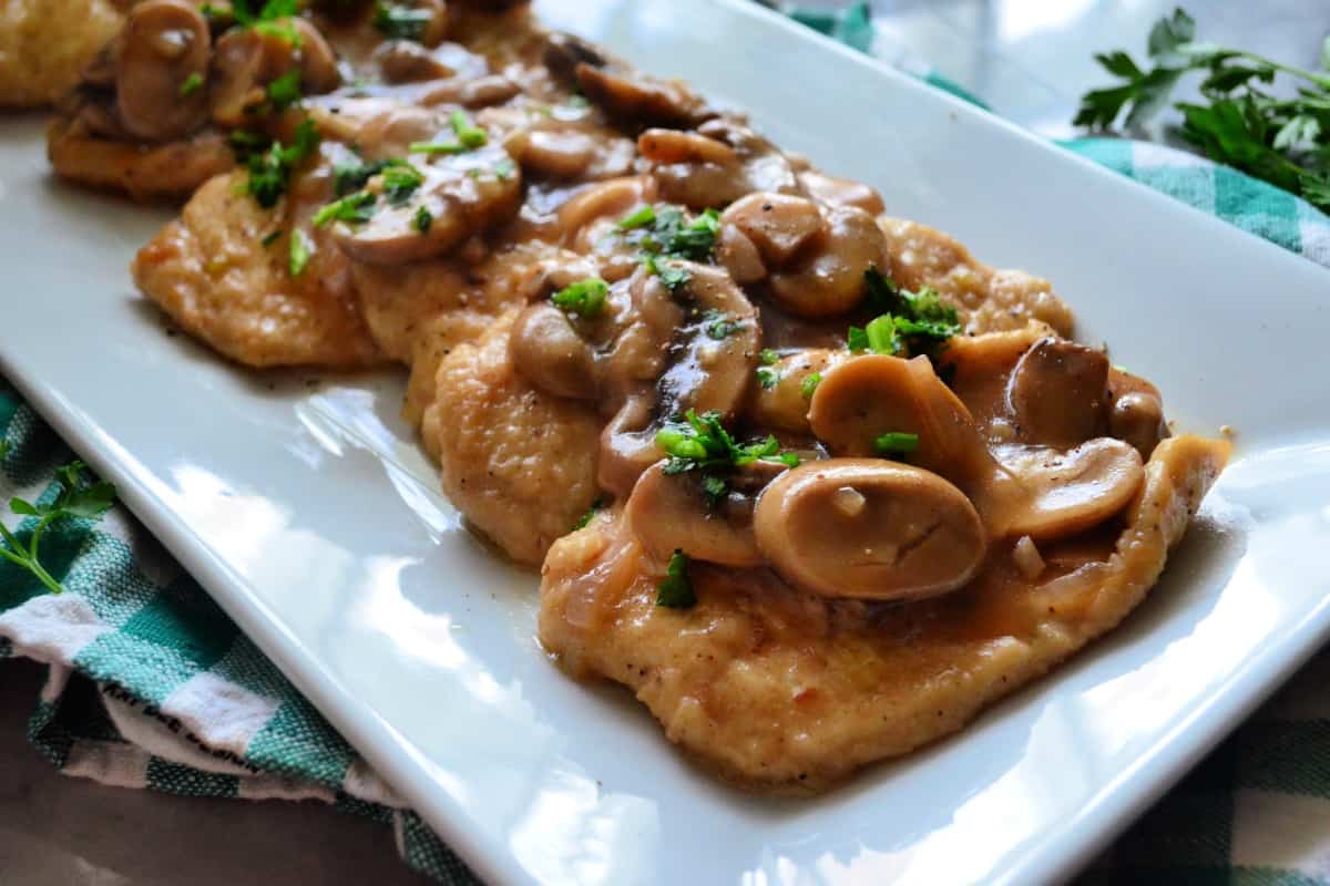 rectangular platter with chicken smothered in brown mushrooms sauce and garnished with parsley.