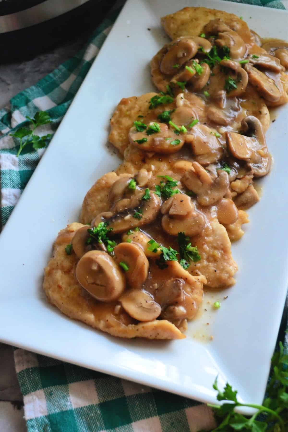 Rectangular platter of chicken covered in brown sauce with mushrooms and parsley garnish.