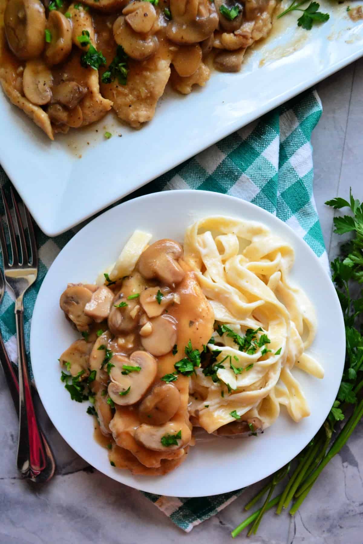 Top view of Chicken Marsala with fettuccine Alfredo on a round plate next to fork.