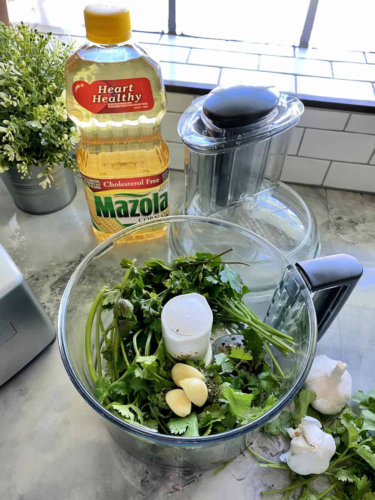 top view of food processor with cilantro, parsley, garlic, corn oil, white vinegar, salt, and pepper in it.