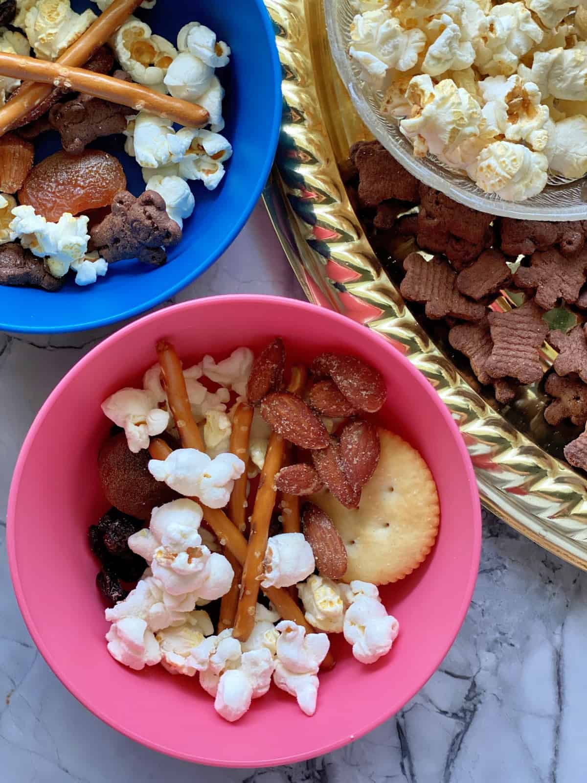 Close up top view of 2 small bowls and side of platter filled with popcorn snack mix on countertop.