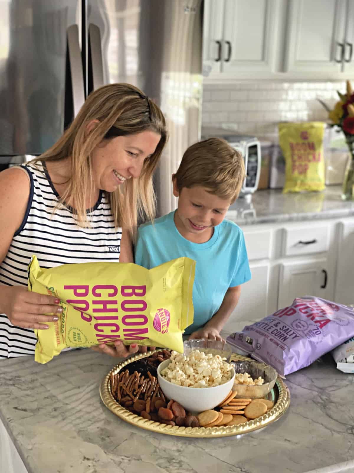 Mother and son pouring Angie’s BOOMCHICKAPOP Sea Salt Popcorn into a bowl at countertop.