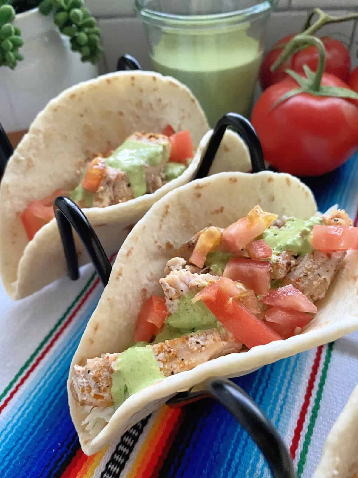 two Swordfish Tacos with Creamy Cilantro Dressing in metal taco holder on striped tablecloth. 