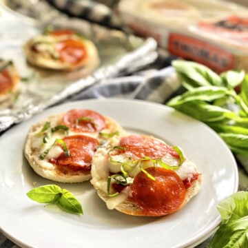 Two Toaster Oven English Muffin Pizzas garnished with basil on a white plate over checkered tablecloth.