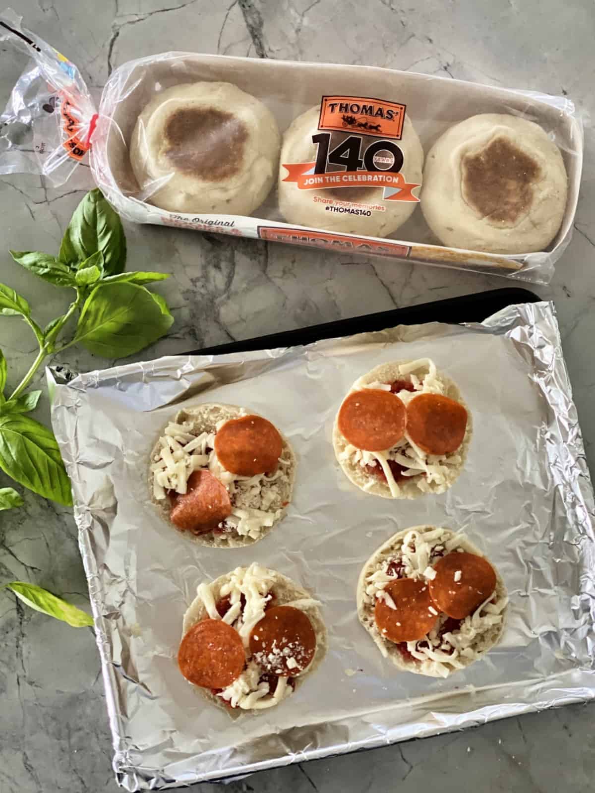 Toaster Oven English Muffin Pizzas assembled on aluminum foil covered pan next to package of Thomas English Muffins.