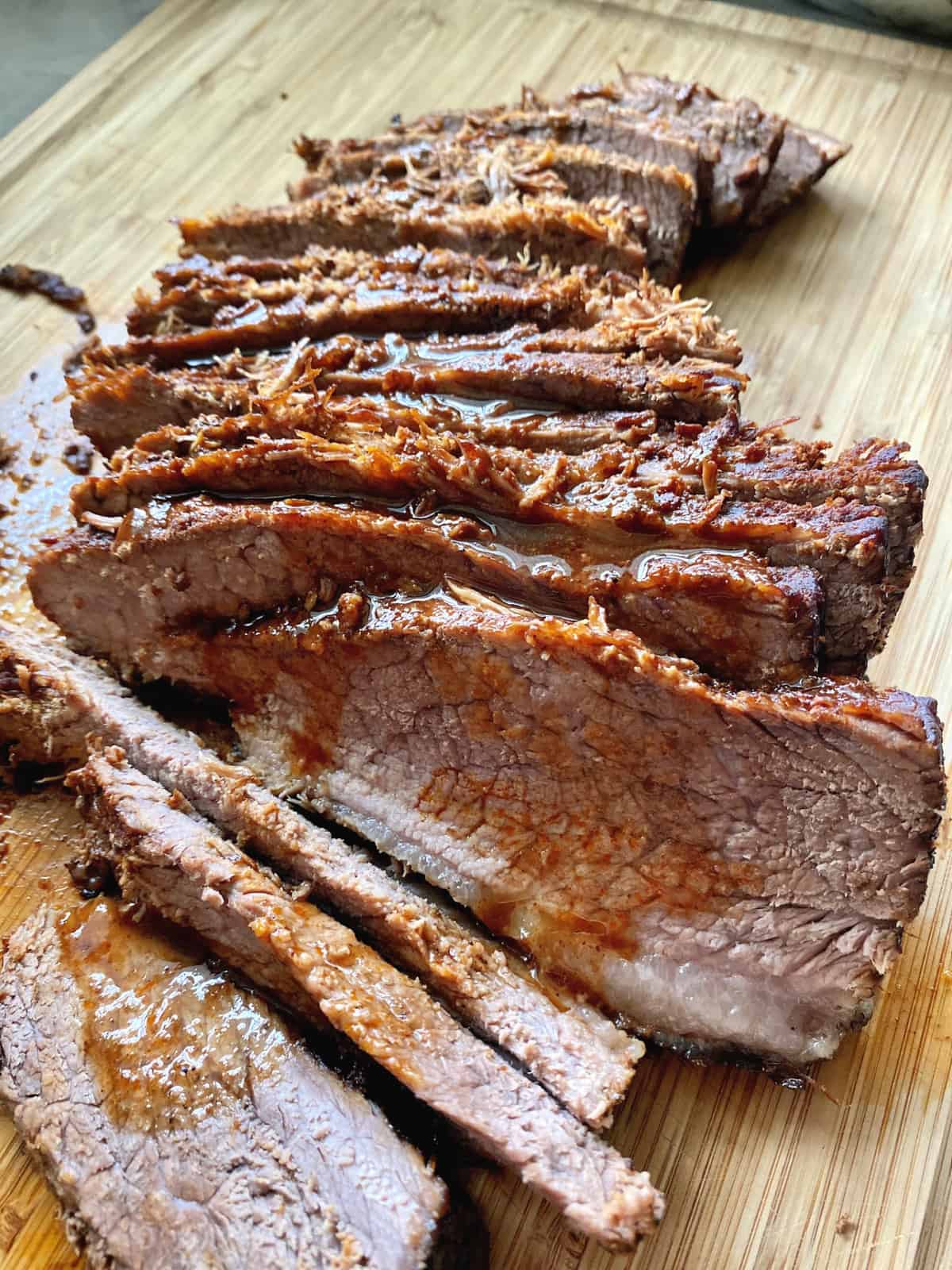 Close up of thinly sliced beef with sauce on a wooden cutting board.