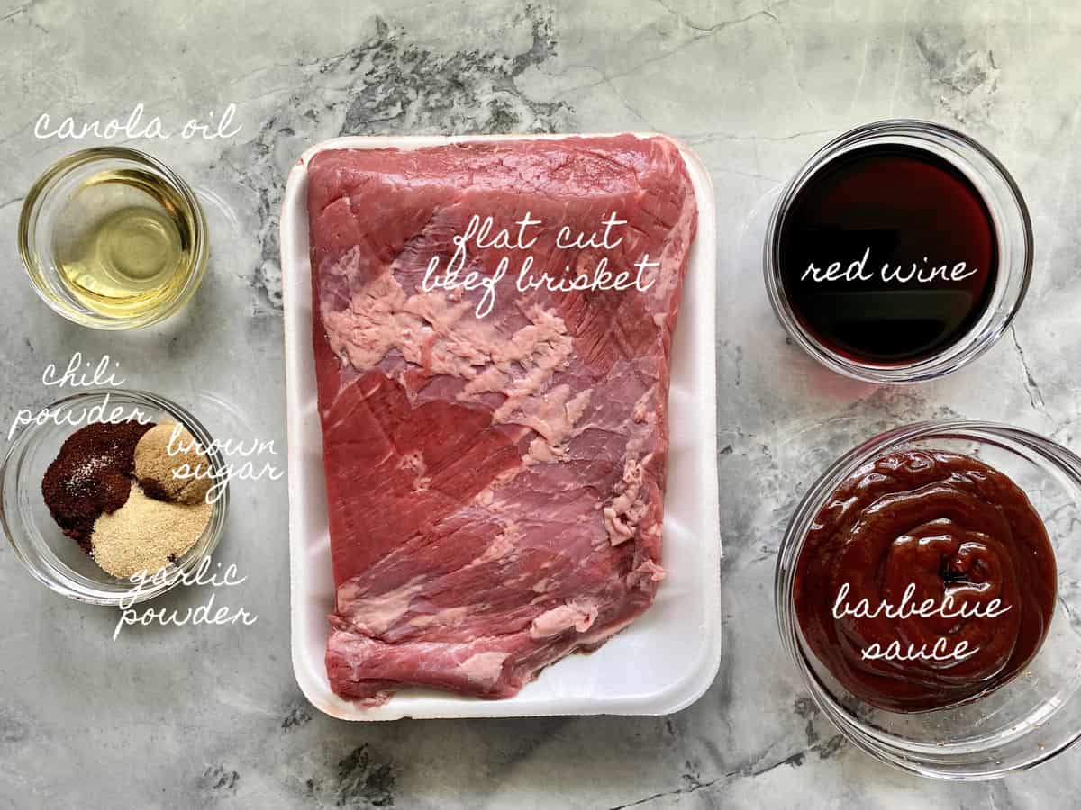 Ingredients on counter; flat cut beef brisket, oil, red wine, barbecue sauce, spices.