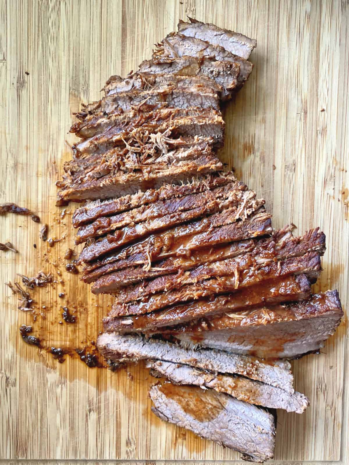 Top view of a full piece of brisket thinly sliced with sauce on top of a cutting board.