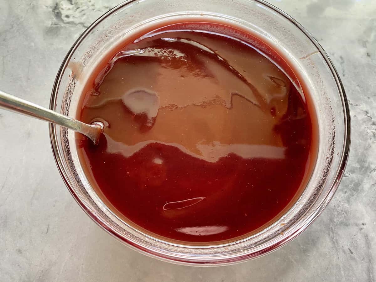 Glass bowl on marble countertop with red wine and barbecue sauce mixed together.  