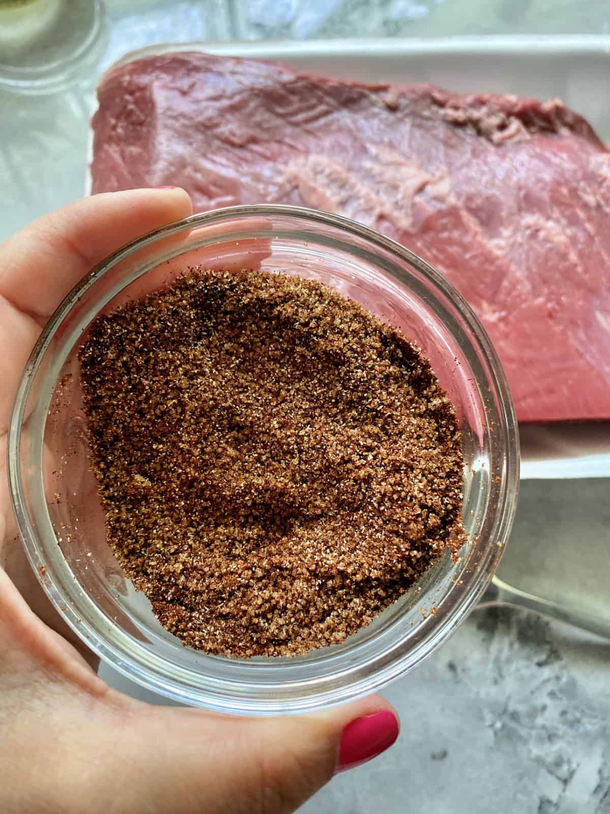 Top view of a pink nail polished hand holding a glass bowl with spices in it. 