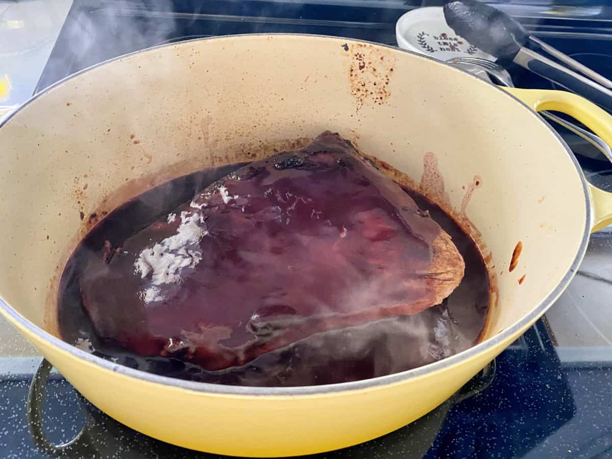 Red sauce poured on top of beef in a yellow cast iron pot on the stovetop. 