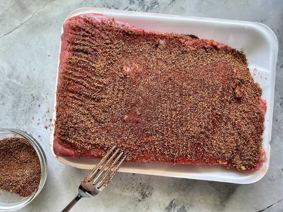 Top view of flat cut raw brisket on a meat try with rub all over it. 