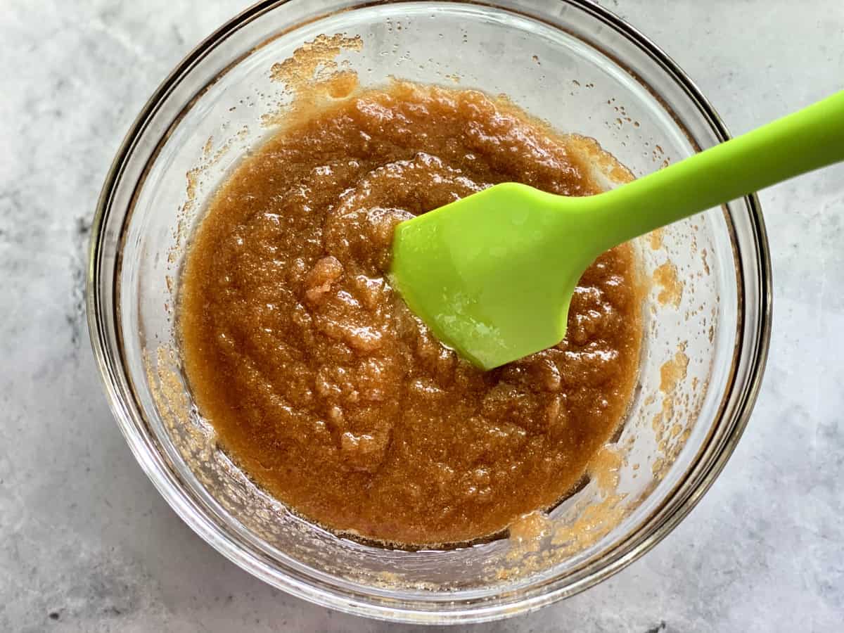 Glass bowl with brown sugar butter mixed with a green silicone spatula.