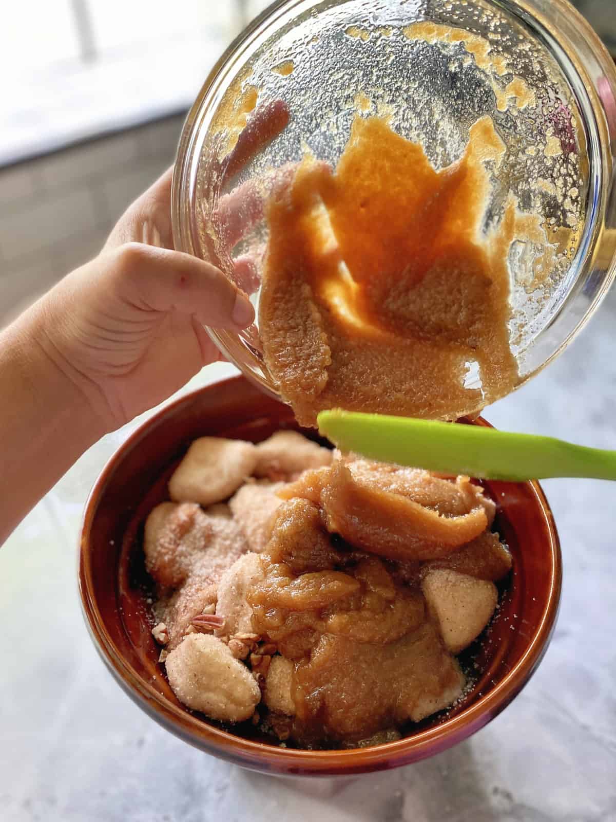 Hand pouring brown sugar glaze from a glass bowl on to fluted pan with dough.