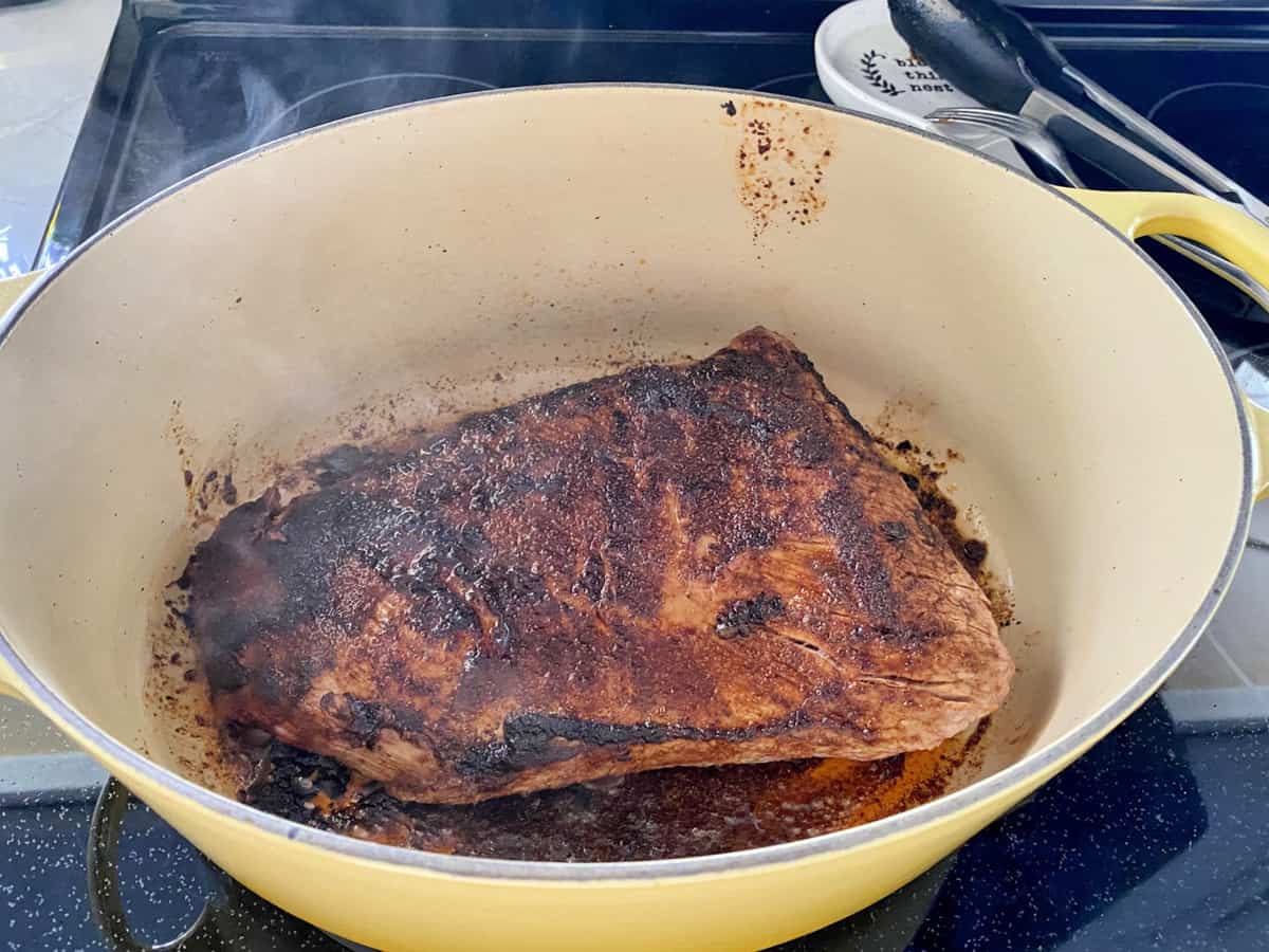 Flat cut brisket searing on stovetop in a yellow cast iron pot. 