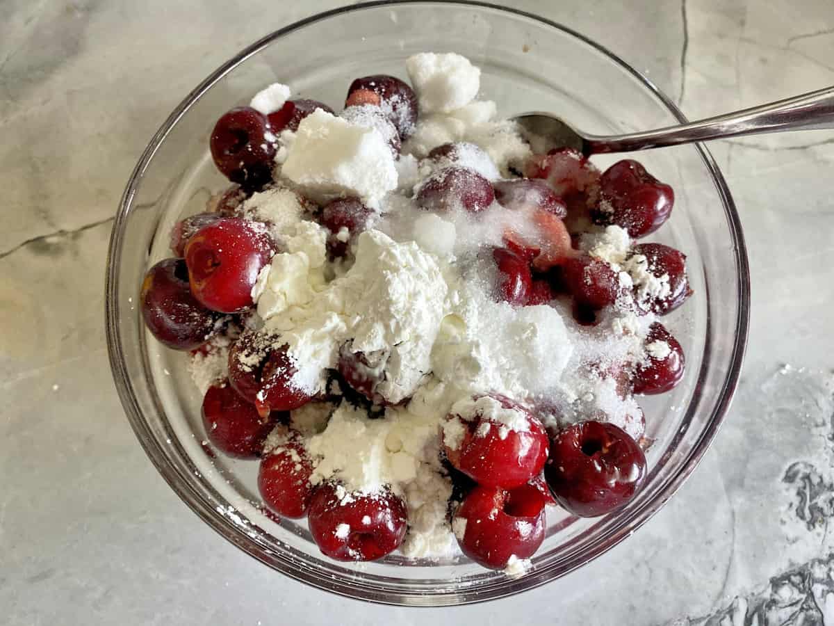 Top view of fresh pitted cherries with sugar and cornstarch in a glass bowl.