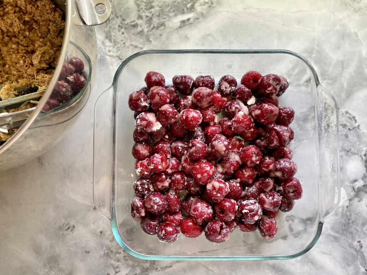 Top view of sugar coated cherries in a glass square pan with crumble in a bowl to the side.