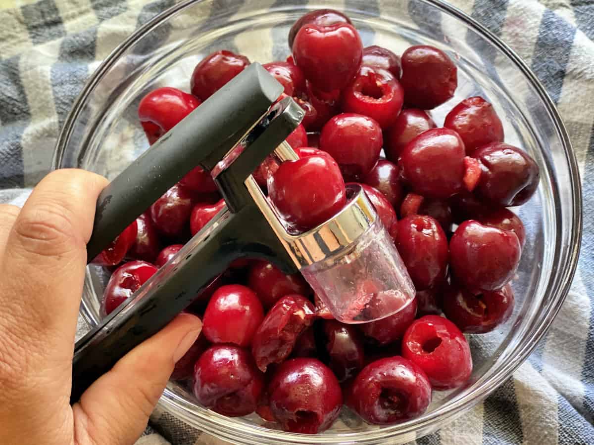 Overhead shot with hand pressing fresh cherry through a pitter into a bowl of cherries.