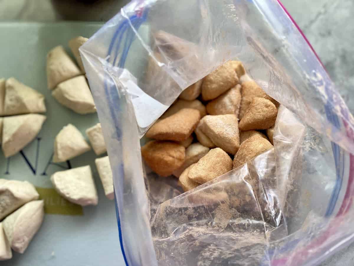 Top view of quartered biscuits tossed in cinnamon sugar in a bag. 