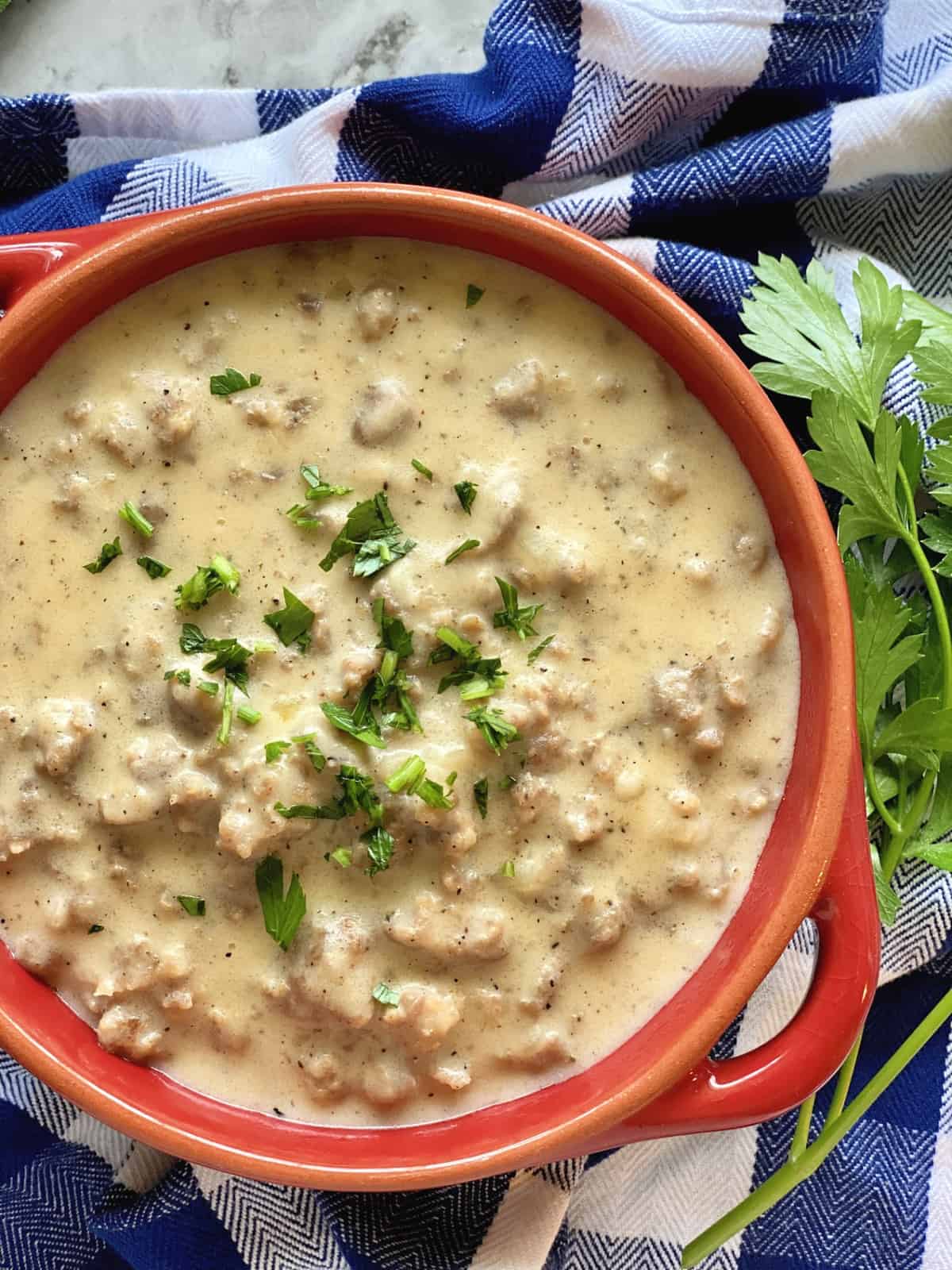 Top view of sausage gravy in a red bowl with fresh herbs.