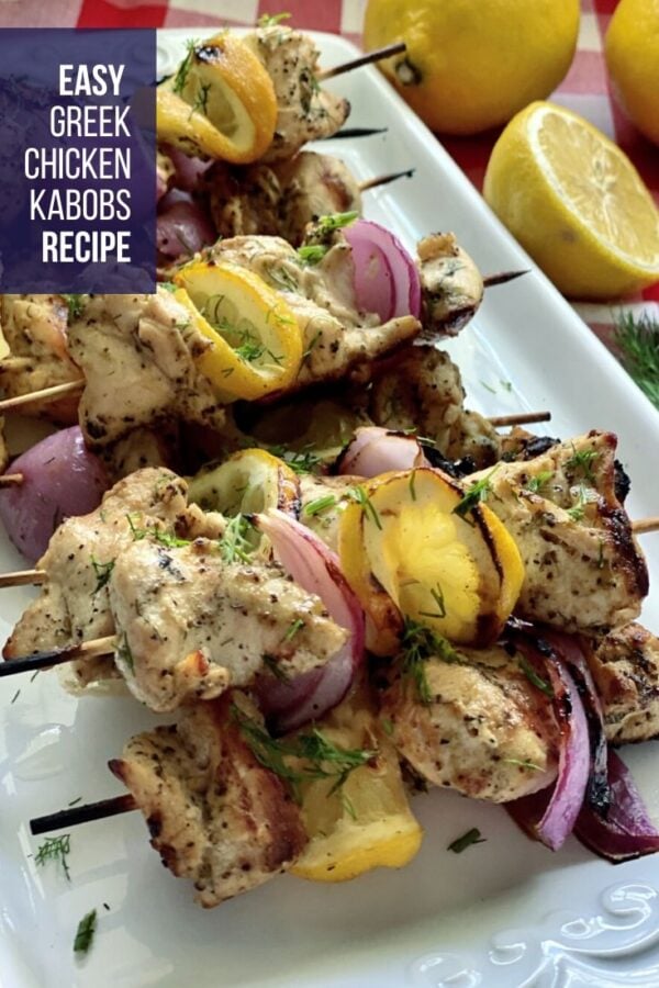 Grilled chicken kabobs on a white platter with lemons in background.