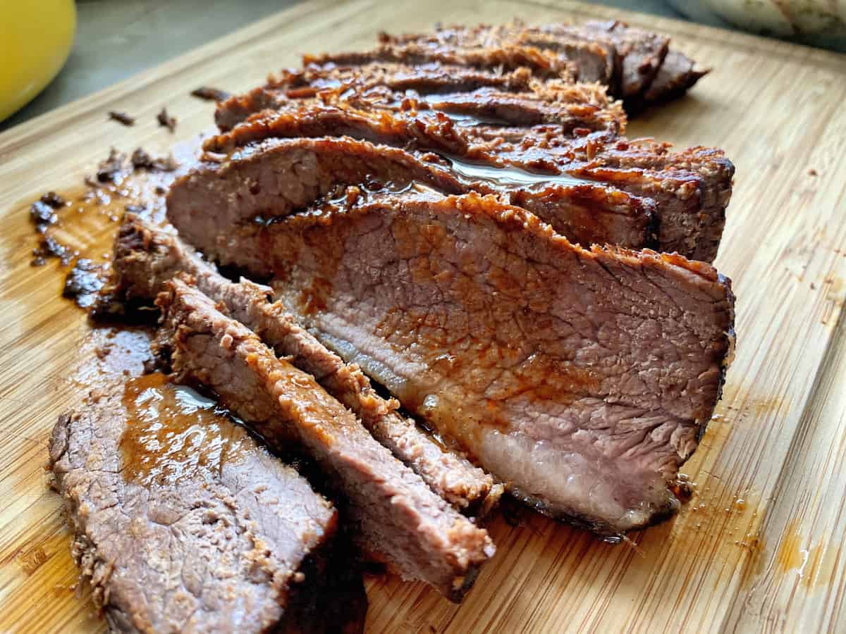 A large stack of sliced juicy beef fanned out on a wooden cutting board. 