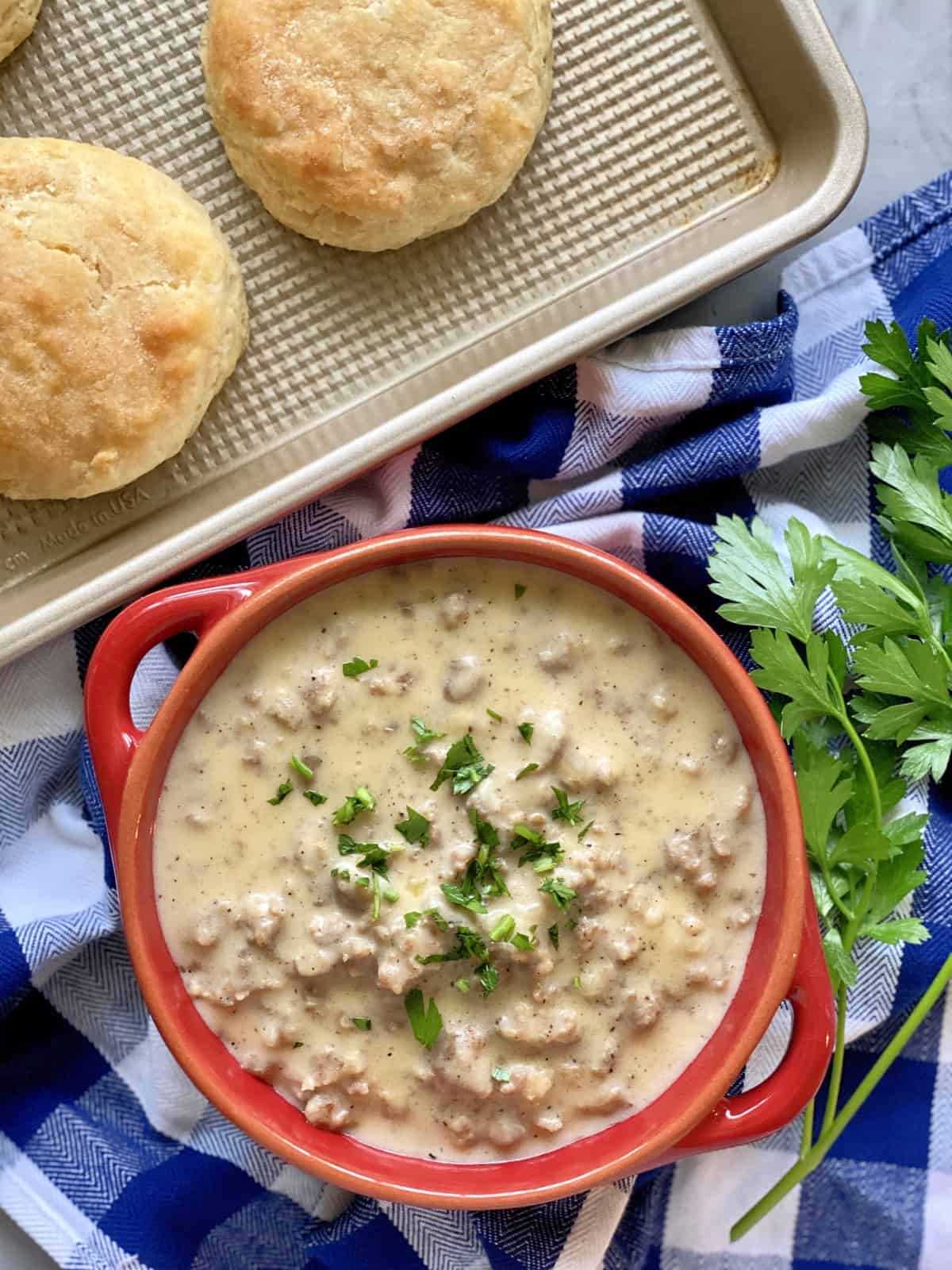 Top view of a bowl of sausage gravy with biscuits on a sheet pan