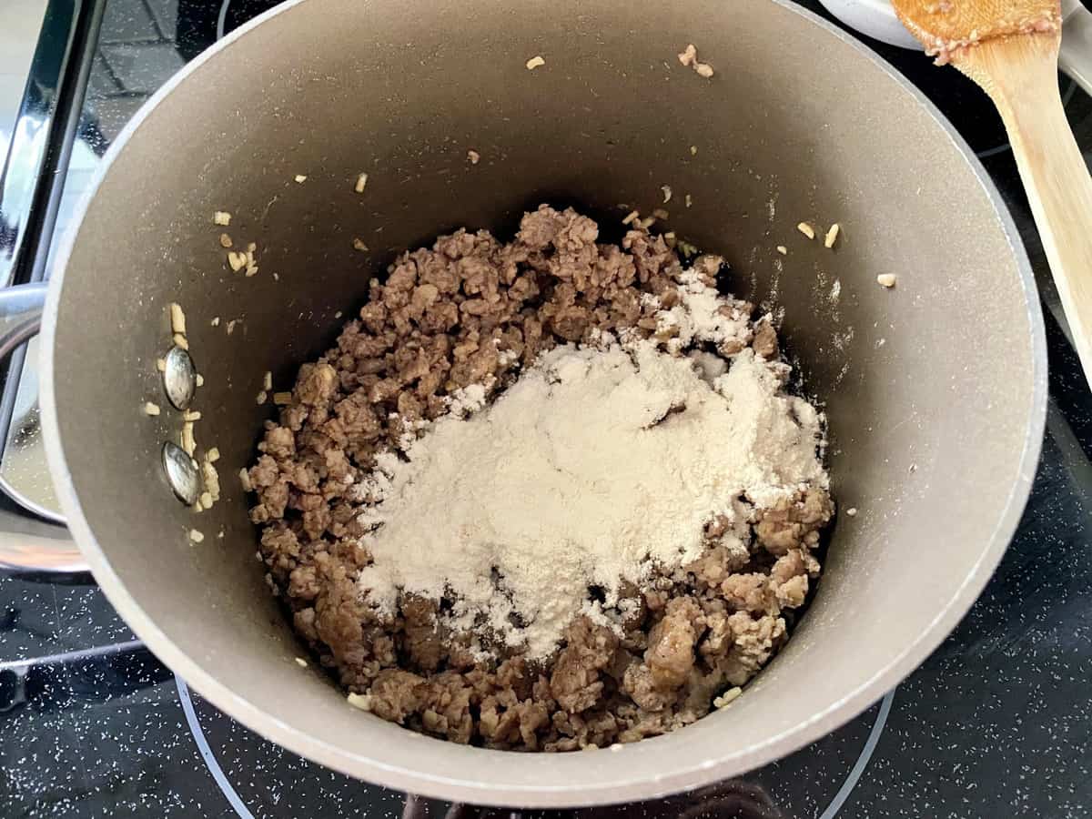 Sauce pan full of ground pork sausage with flour sprinkled on top.