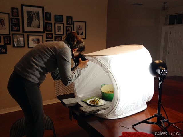 Blogger photographing food in a white lightbox tent with artificial lighting.