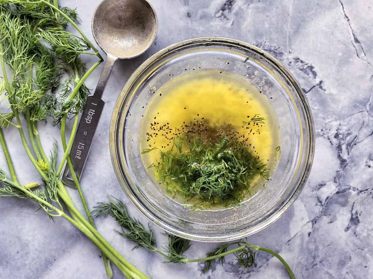 Butter, seasoning, and fresh dill in a glass bowl on a grey marble countertop.