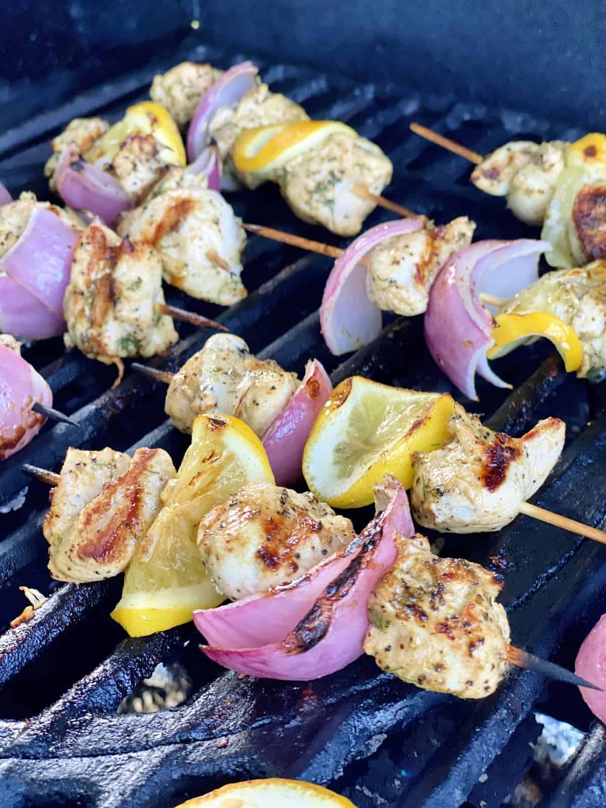 Chicken, red onion, and lemon skewers cooking on the grill. 