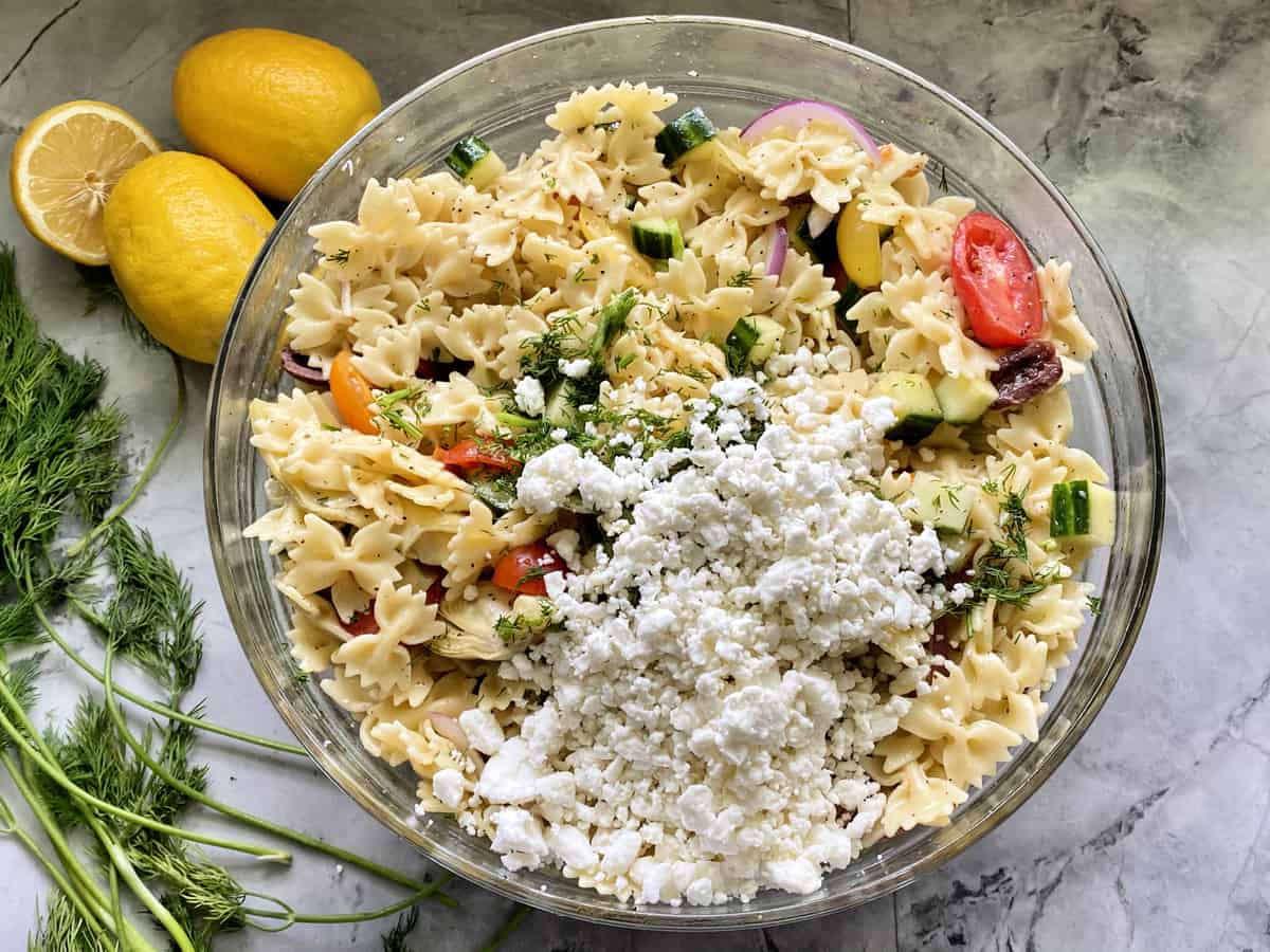 Top view of a bowl of bow tie pasta with vegetables and feta cheese sprinkled on top.