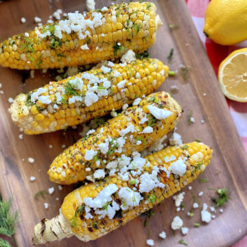 Top view of grilled corn on a wood platter with feta and dill.