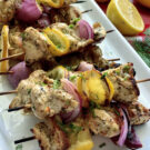 Chicken, red onion, and lemon on wood skewers on a white plate with fresh dill.
