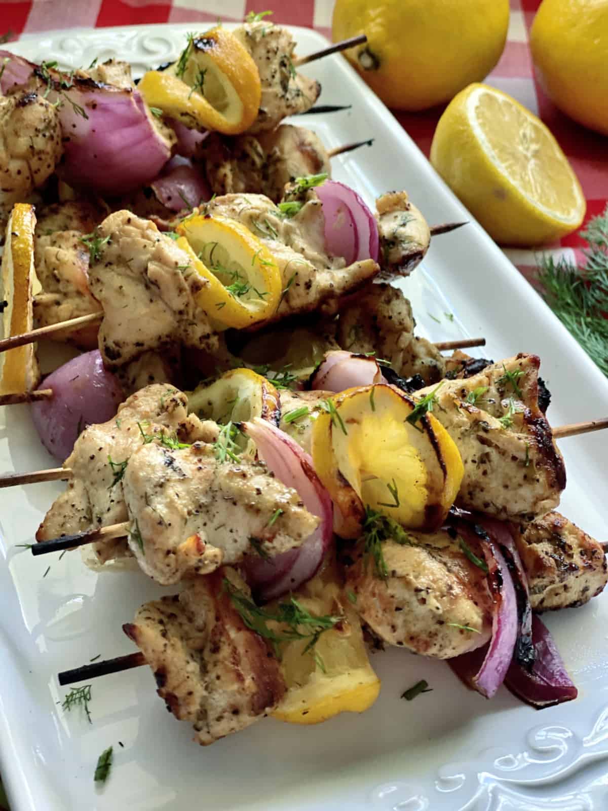 Chicken, red onion, and lemon on wood skewers on a white plate with fresh dill.