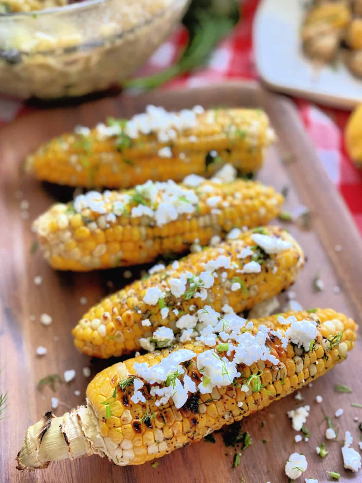 Corn on the cob on a wooden platter with feta crumbles and fresh dill.