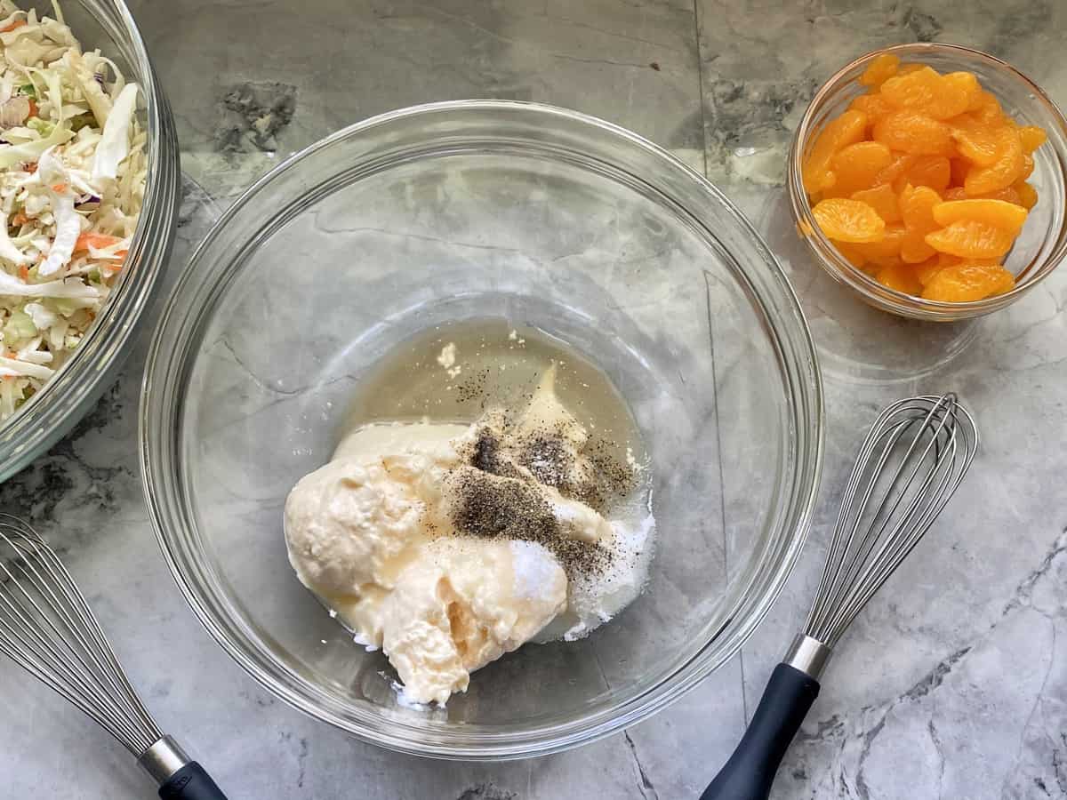 Top view of glass bowl with mayonnaise, salt, pepper, vinegar, and sugar with whisk.