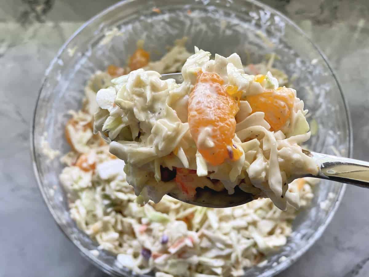 Glass bowl on counter with a raised spoon full of coleslaw with oranges on it.