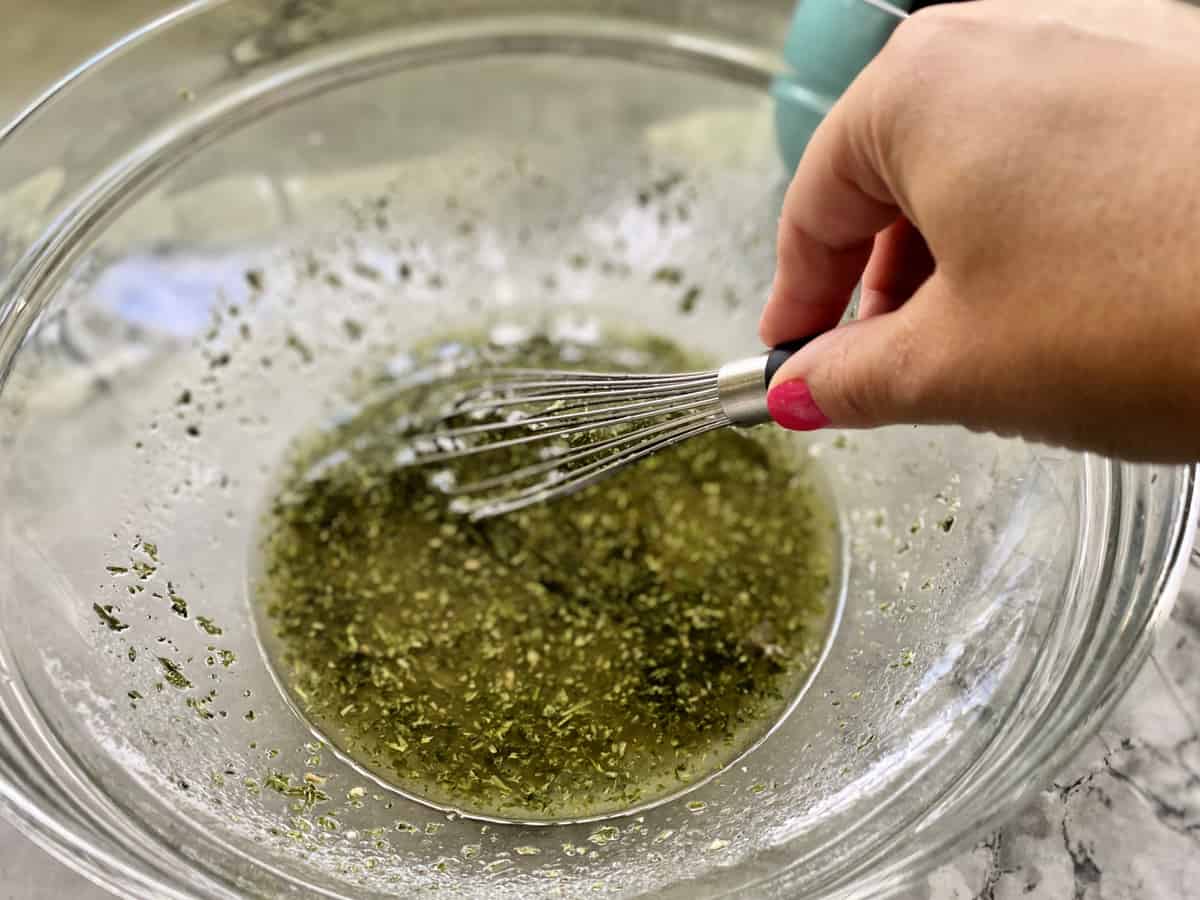 Hand with pink nails whisking parsley dressing in a glass bowl. 