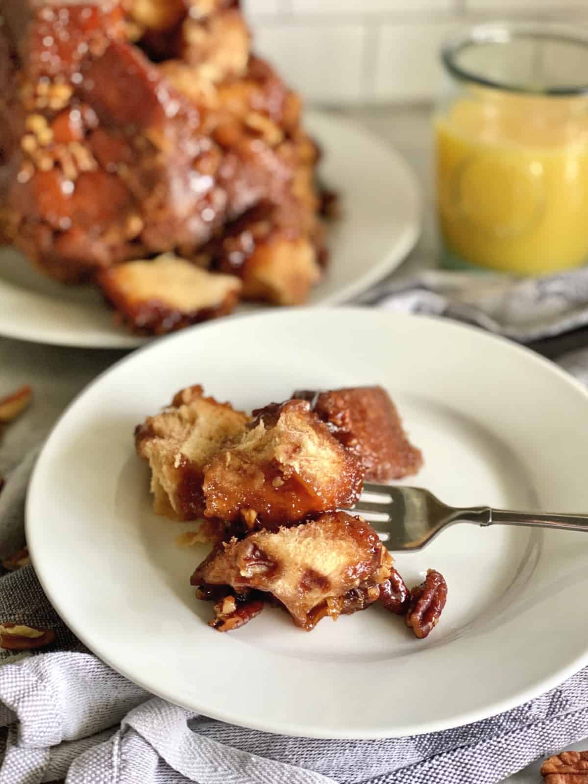 Pulled apart sweet bread on a white plate with a fork with oj in background.