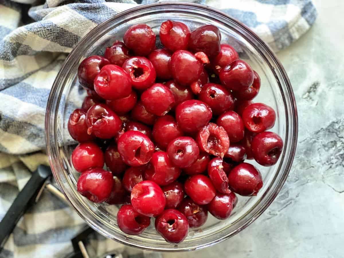 Top view of pitted fresh cherries on a marble countertop with blue and white dishcloth.