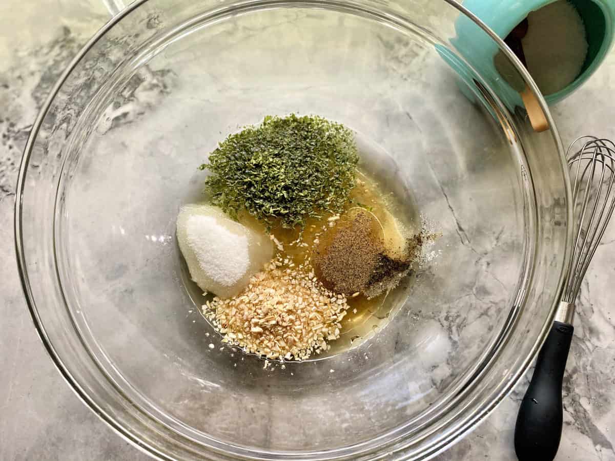 Top view of a glass bowl with parsley, sugar, oil, pepper and onion. 