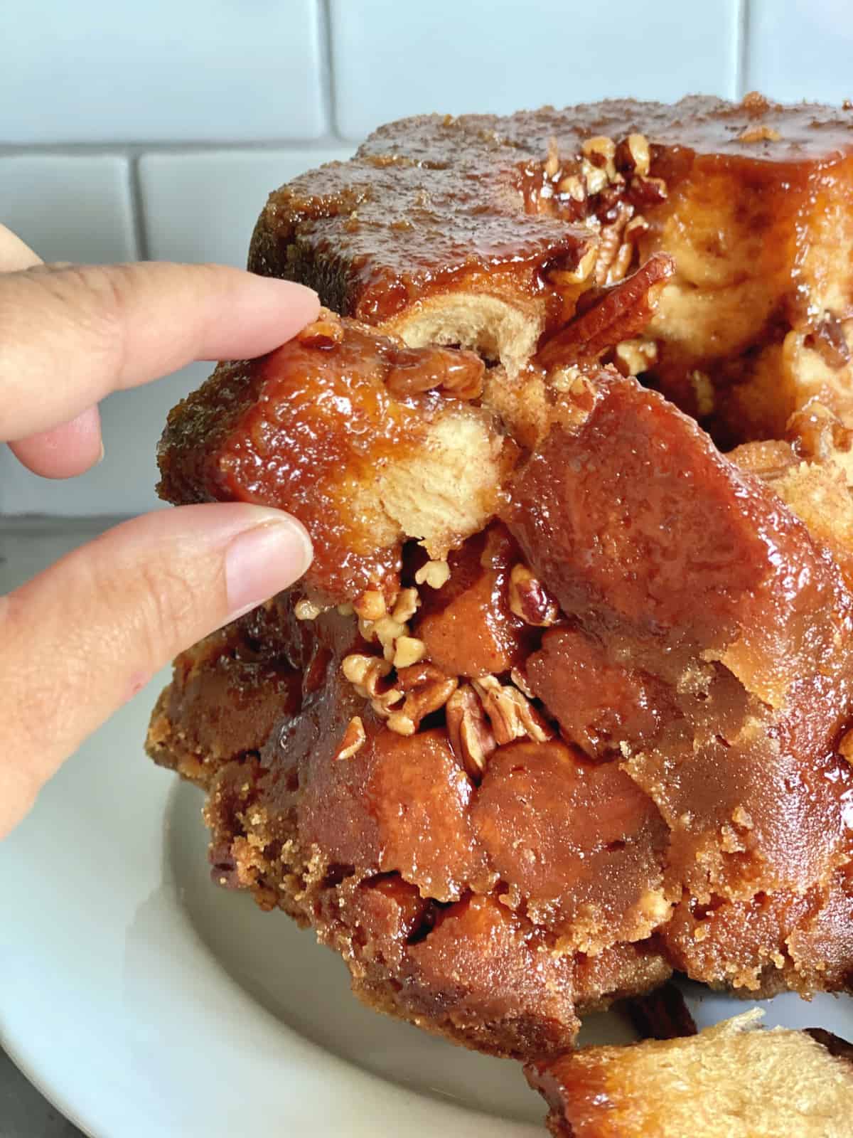 Fingers pulling apart sticky pull apart bread with pecans. 