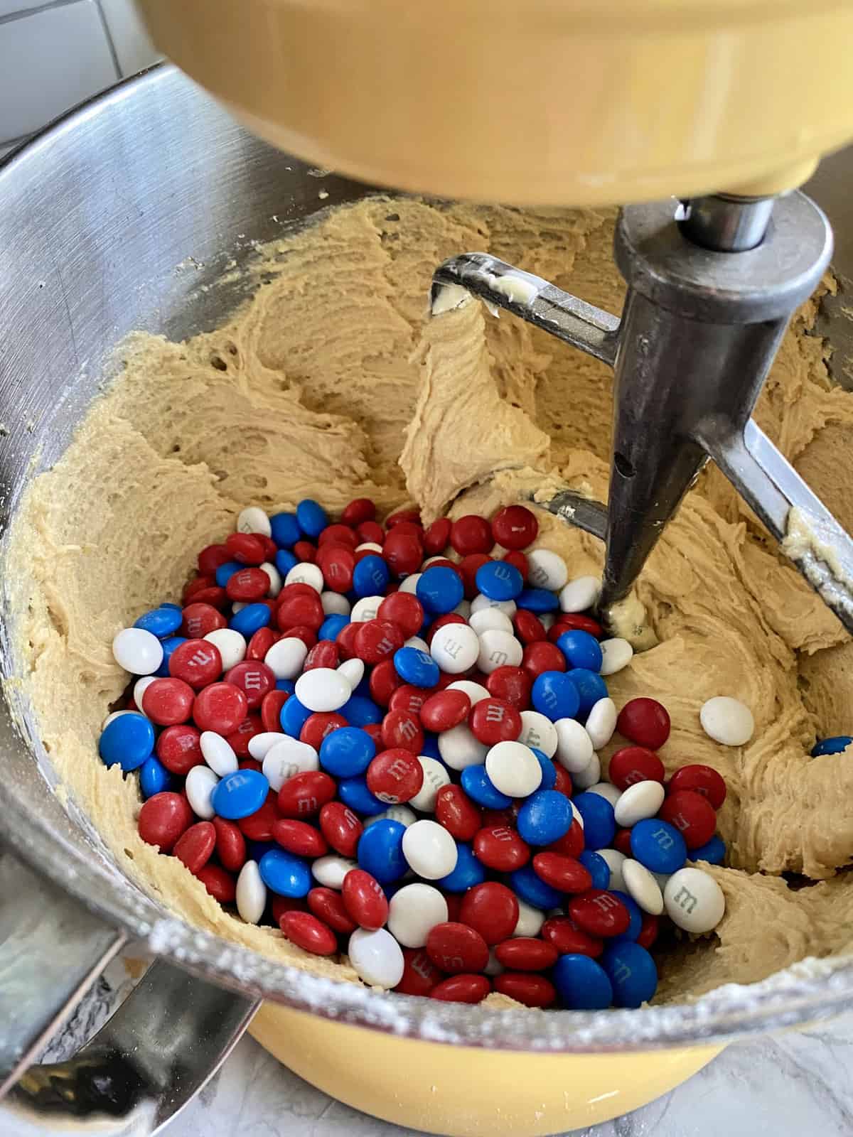 Red, white, and blue M&M's on tot of cookie dough  in a stand mixer.