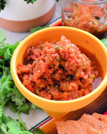yellow bowl filled with salsa with cilantro and chips on the side.