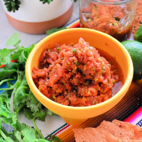 yellow bowl filled with salsa with cilantro and chips on the side.