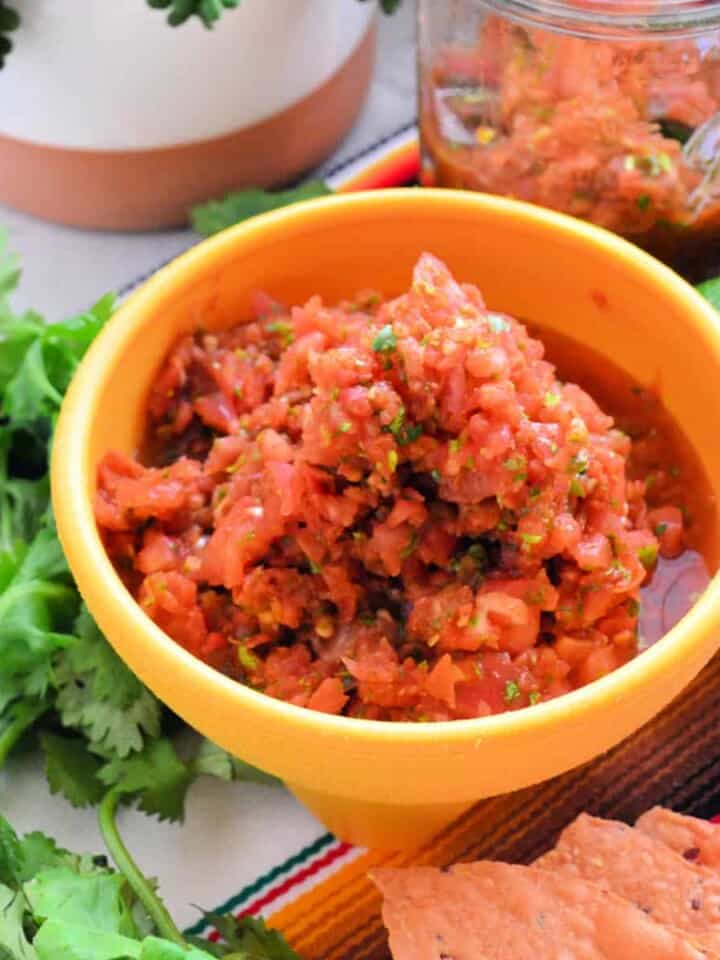 yellow bowl filled with salsa with cilantro and chips on the side.