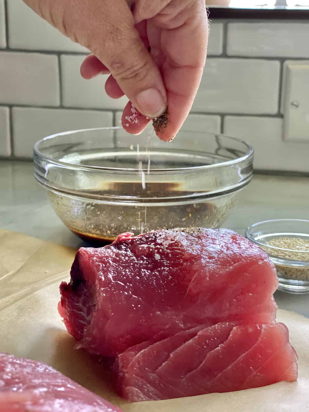 Female hand seasoning fresh yellowtail tuna with salt and black pepper. 