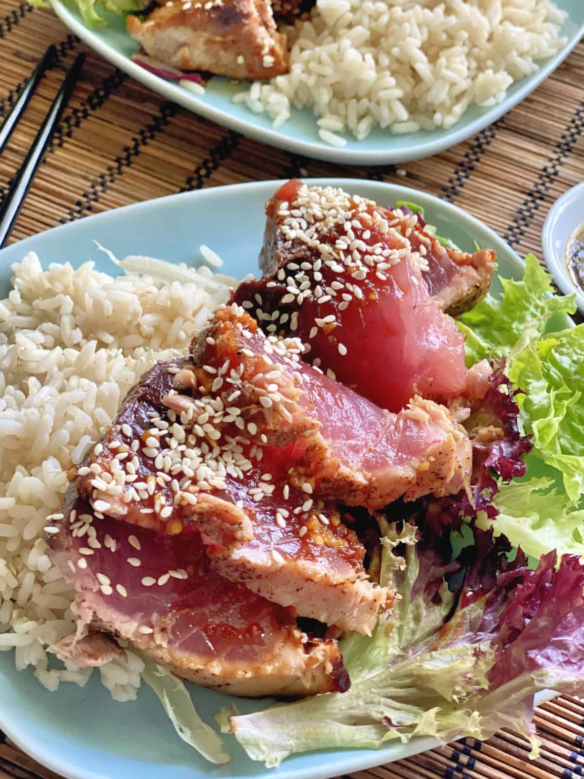 Up close view of sliced tuna with sesame seeds on top of a bed of salad and rice.